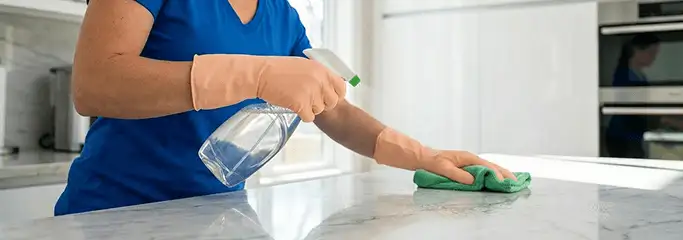 Maid service worker spraying and wiping a kitchen countertop with a microfiber cloth for sanitizing, Reno, NV.