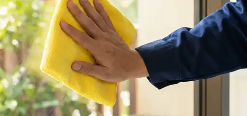 House cleaner wiping a glass window with a yellow microfiber cloth for streak-free cleaning, Reno, NV.